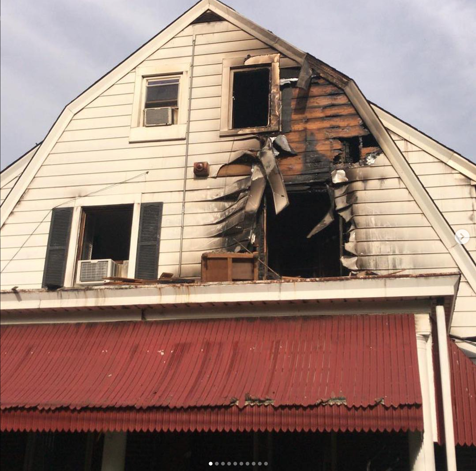 Fire damage to a house with a red awning. Charred siding and broken windows are visible.